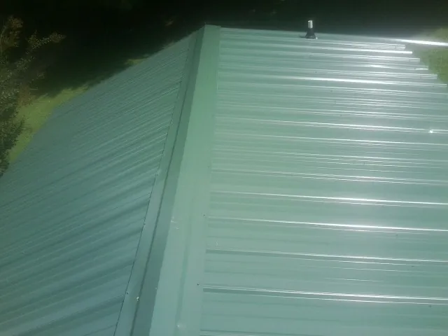 New green metal panels meeting at the ridge of a roof — Flat Roof Repair work by our crew in Paulsboro