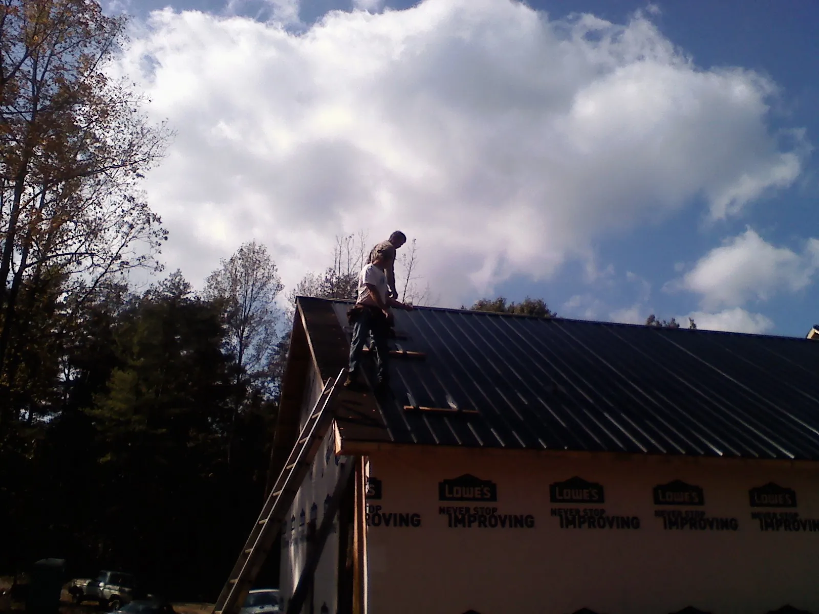 Roofer fastening dark metal panels high against a cloudy sky, from a Roof Inspection job in Paulsboro