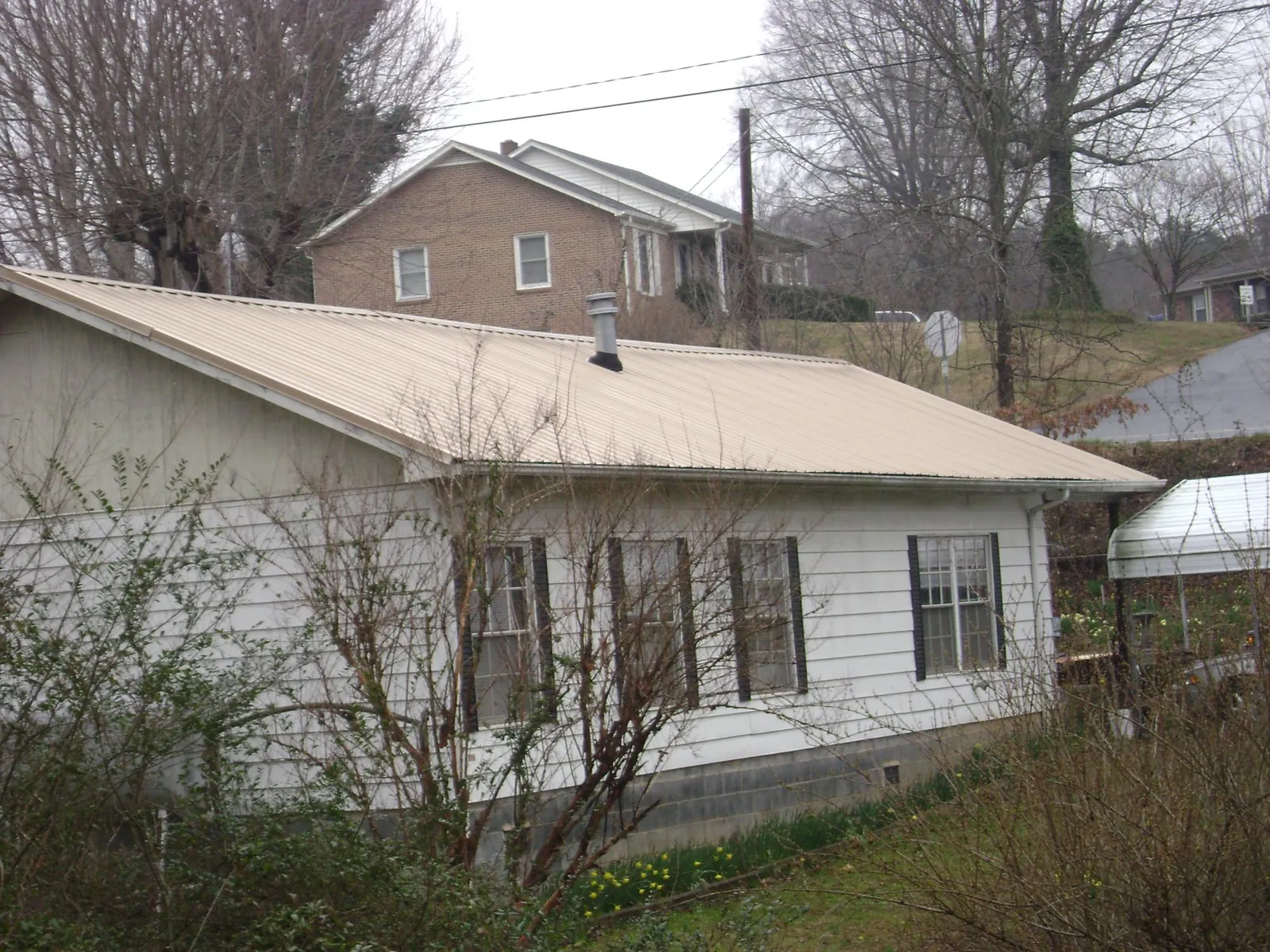 Tan metal roof on a white sided house set into a hillside — Commercial Roofing by Roofing Brothers in Paulsboro